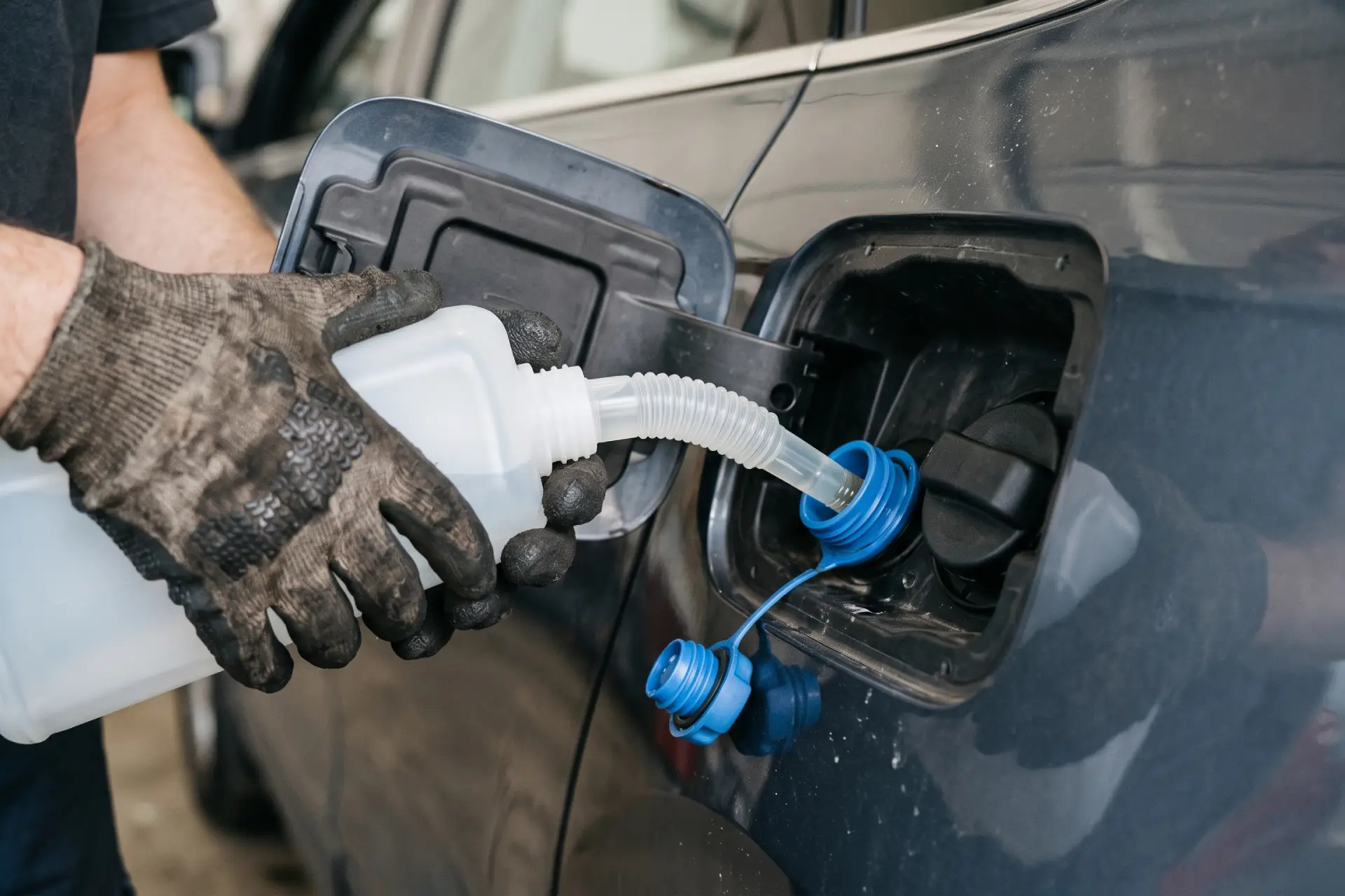 Meccanico che sta riempiendo il serbatoio dell'AdBlue di un'automobile diesel tramite una tanica dotata di un apposito tubo flessibile di travaso